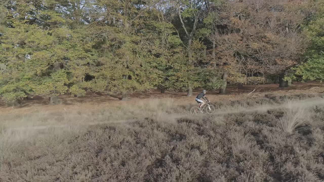 foto de un dron lateral de un ciclista de montaña montando cuesta arriba en la naturaleza