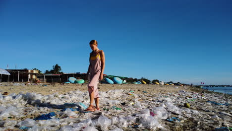 tan caucasian blonde girl walking alone on dirty polluted beach, plastic ocean trash