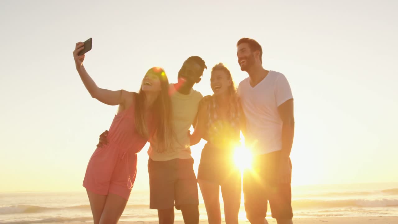 젊은 성인 친구들이 해가 지는 해변에서 4k를  ⁇ 고 있습니다.