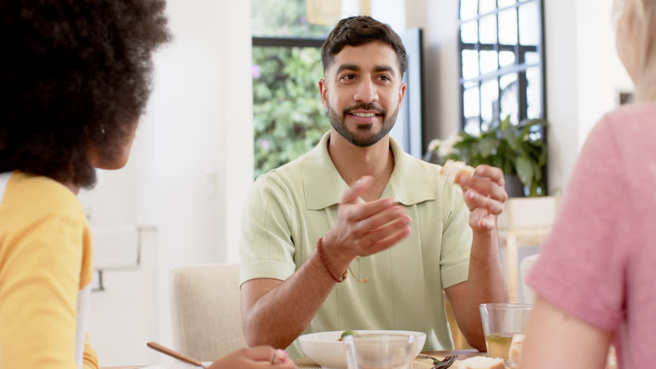 Friends having conversation while eating lunch together at home dining table