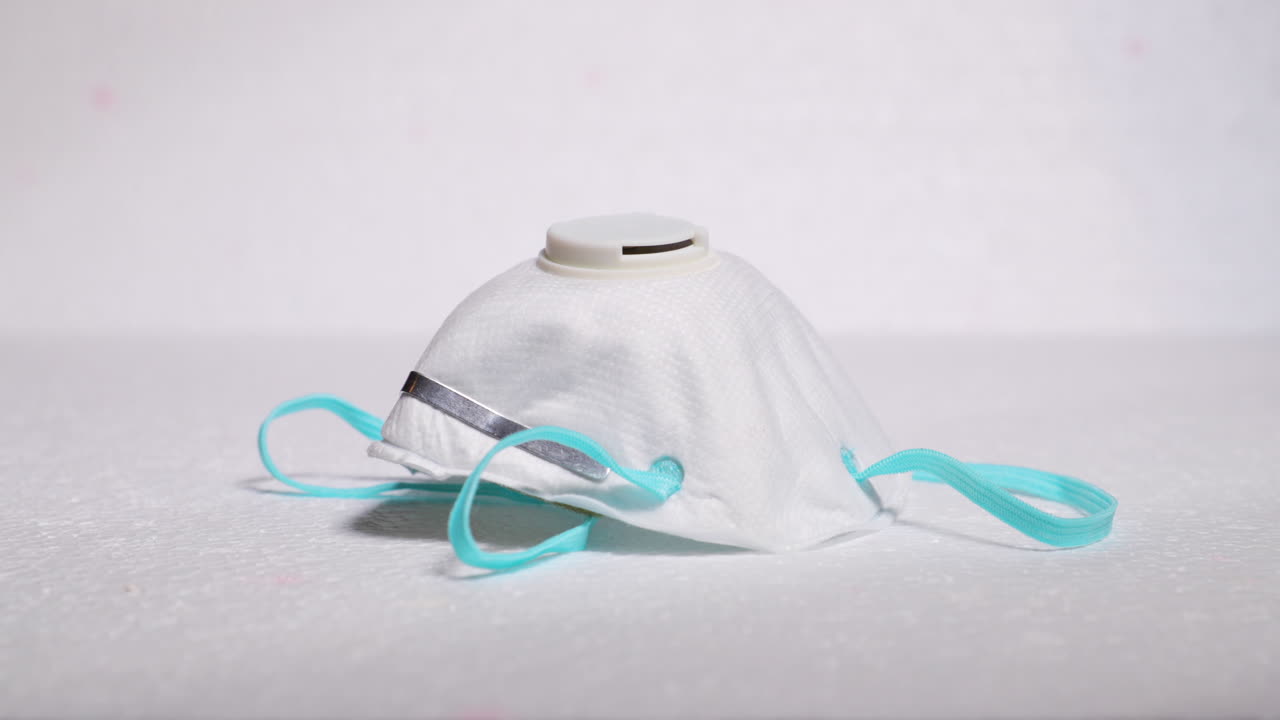 Hand putting protective facial white mask mask against threat like corona covid-19 virus on white backing protecting mouth and nose on plate capture in 4k 60fps