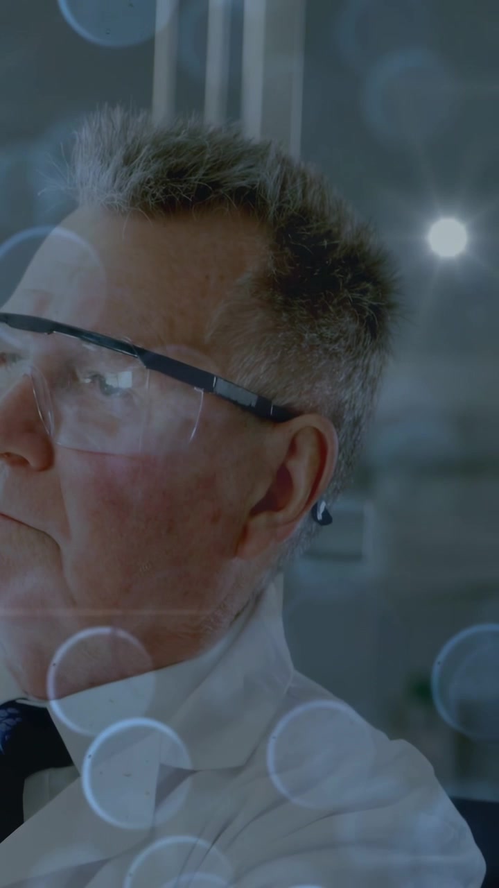 Video verticale: Medico anziano che si gira mentre la telecamera si avvicina, mostrando gli occhiali protettivi, con effetto bokeh per l'esame.