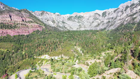 aerial drone footage of beautiful ouray colorado pine tree forest and mountain range with cars driving on highway 550 by rocky mountain houses