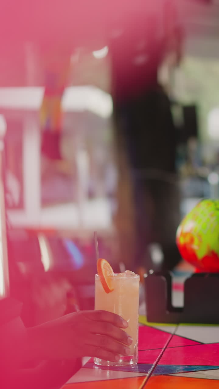 una mujer espera un cóctel en la encimera de un bar. un camarero negro pone paja en la bebida empujando el vaso a una dama atractiva. el camarero sirve una bebida