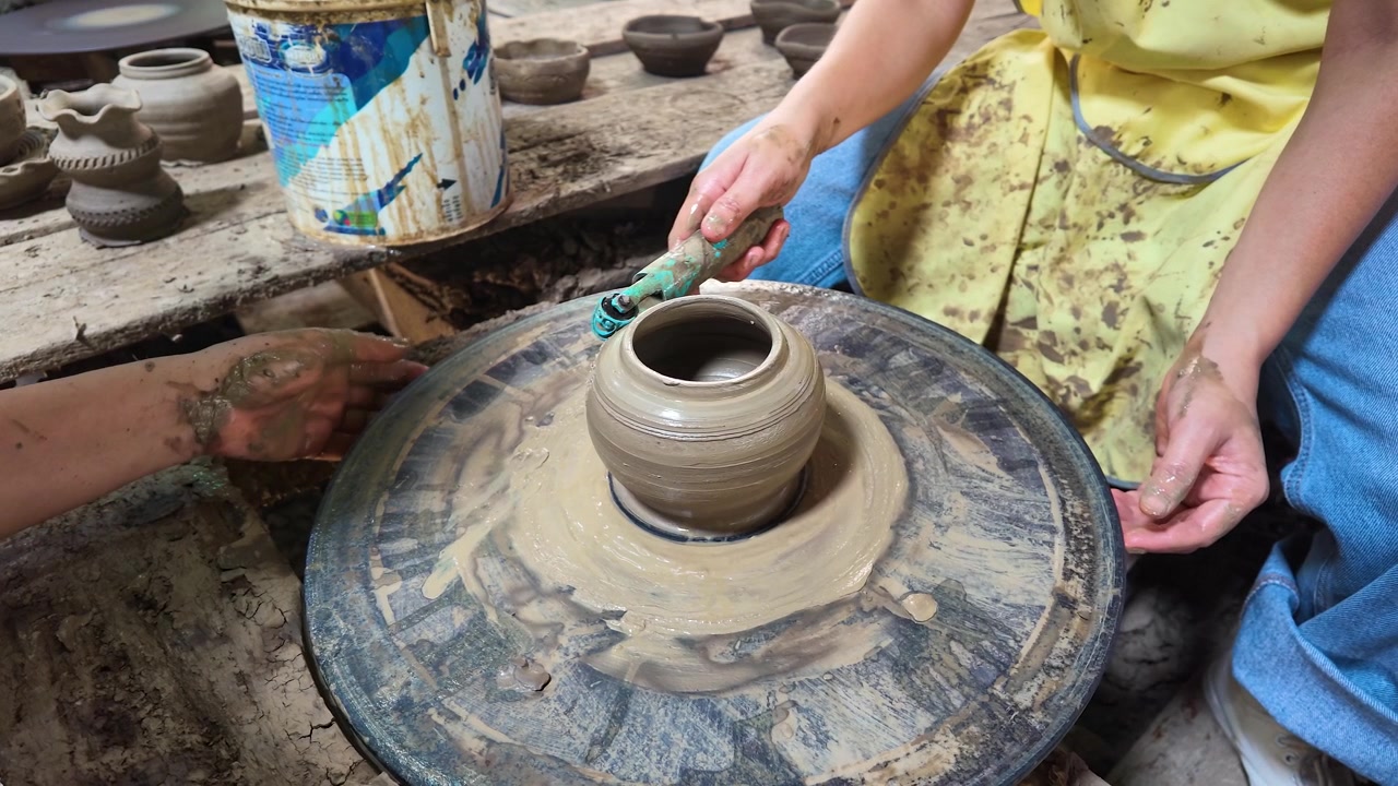 Primo piano di mani che usano un attrezzo per modellare un vaso di ceramica su un tornio