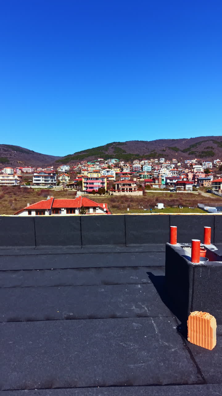 Workers perform maintenance on top of a building while the town sits below in clear weather on a sunny day