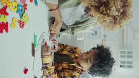 little black boy filling in coloring page with assistance of loving mother
