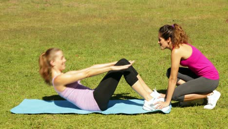 woman doing sit ups in the park with her trainer