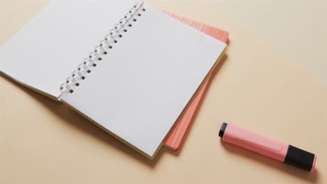 Close-up-of-open-notebook-with-pink-marker-on-beige-background,-in-slow-motion