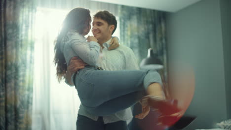 Happy-couple-hugging-in-hotel-room.-Smiling-man-spinning-around-woman-on-hands.