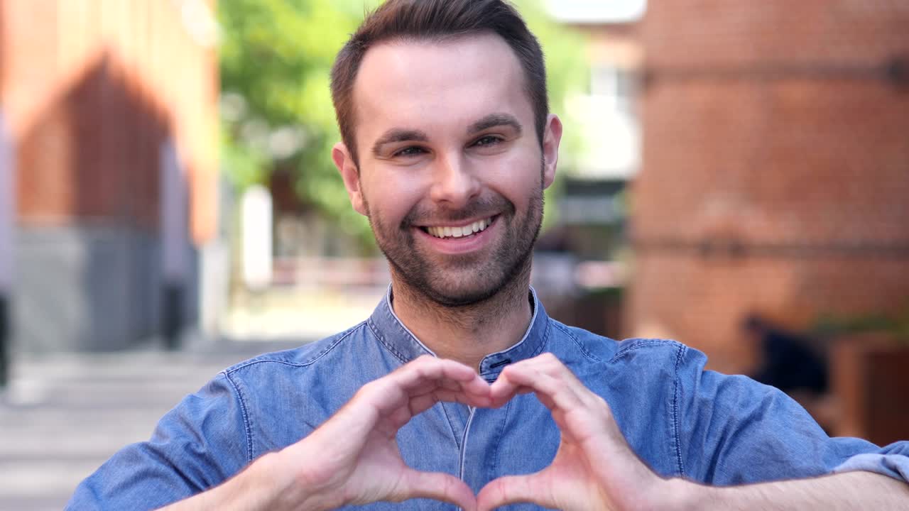 retrato de un hombre casual sonriente gestando el corazón con la mano