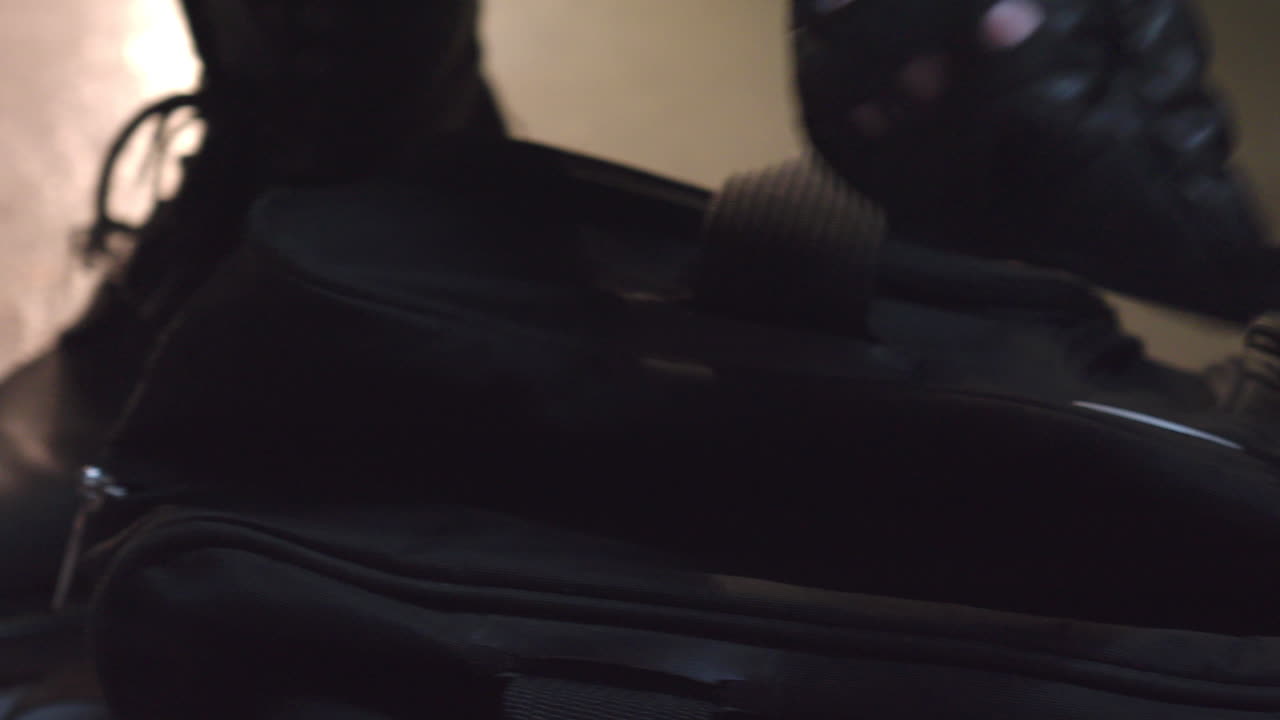 primer plano de las manos con guantes de cuero negro abriendo la cremallera de la bolsa