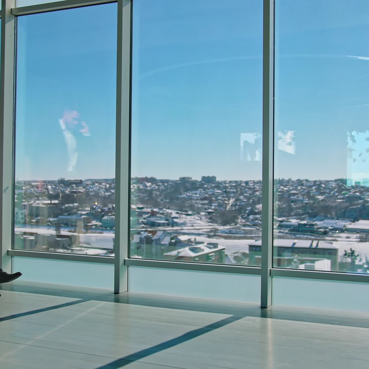 Full-length portrait of businessman. Male entrepreneur in elegant suits walking in modern office and talking about business at his smartphone. Panoramic windows view on city