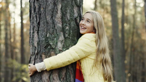 vista cercana de una linda adolescente abrazando un tronco de árbol con los ojos cerrados en el bosque