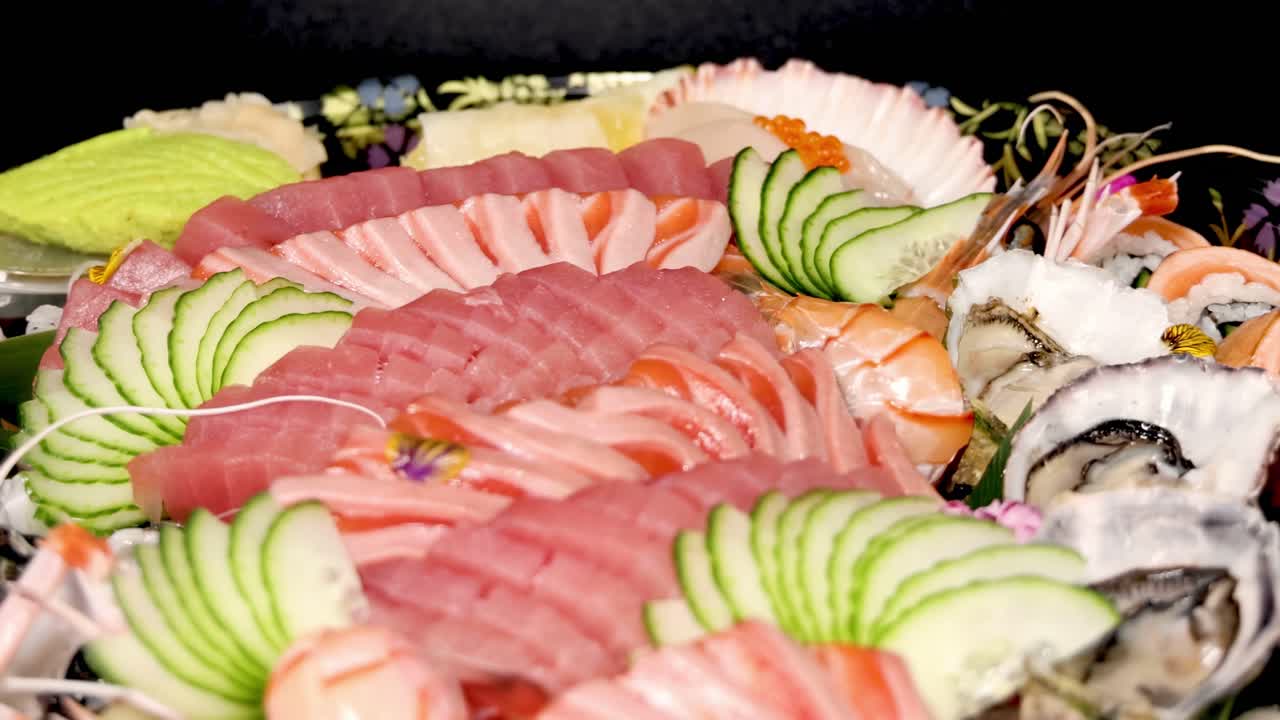 Close-up of a colorful sushi platter featuring sliced tuna, cucumber, shrimp, and decorative flowers.