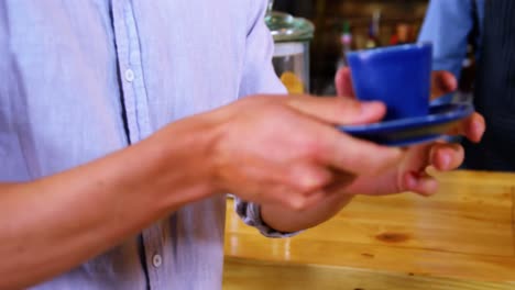 Mid-section-of-waiter-serving-coffee-to-male-costumer-at-counter