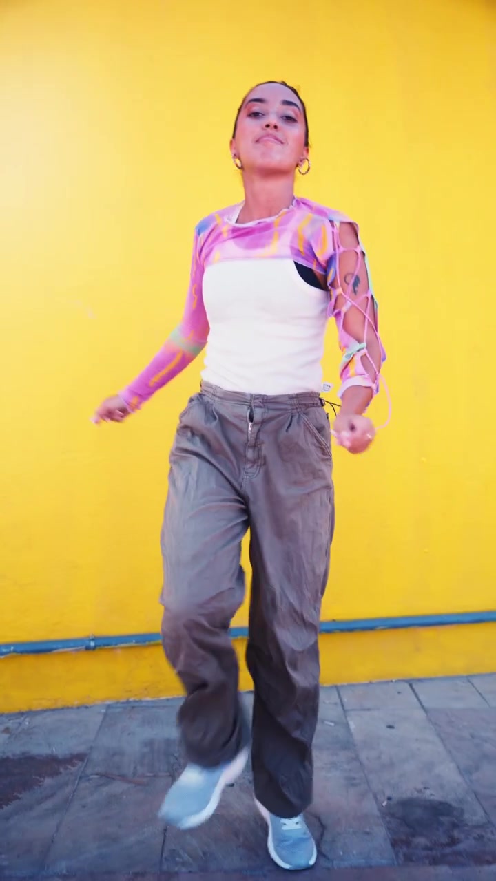 Young Woman Dancing Energetically Against a Vibrant Yellow Wall