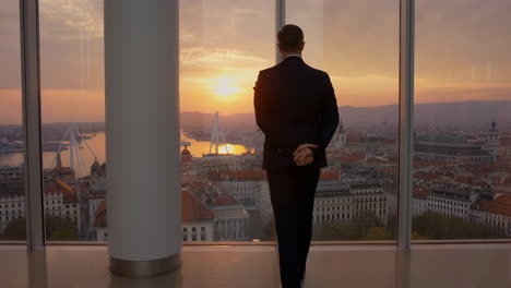 man in suit looking out over city at sunset