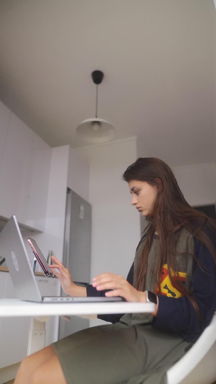 Woman working at a kitchen table with a laptop and tablet