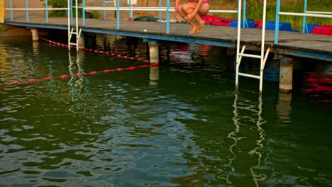 the girl is jumping to the lake from the jetty