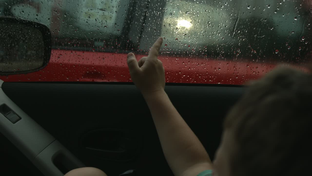 Child looking out car window on a rainy day