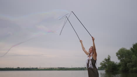 a young girl artist shows magic tricks using huge soap bubbles. create soap bubbles using sticks and rope at sunset to show a theatrical circus show