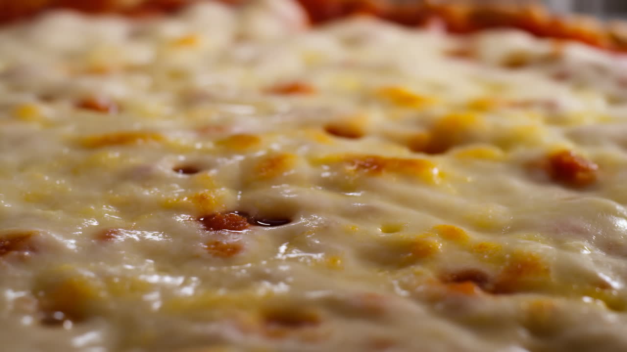Detailní záběr povrchu roztavené sýrové pizzy ukazující táhnoucí se mozzarellu bublající přes zlatavou kůrku pod teplým osvětlením.