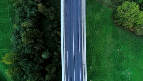 aerial view over a highway road in france. only grass fields and trees around the roads. cars and trucks driving on the roads under the sun.