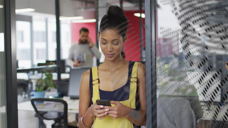 animation of world map over happy biracial businesswoman using smartphone at casual office