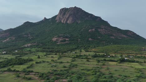 aerial drone shot of mountain with greenery surrounding it with a cloudy skyline.