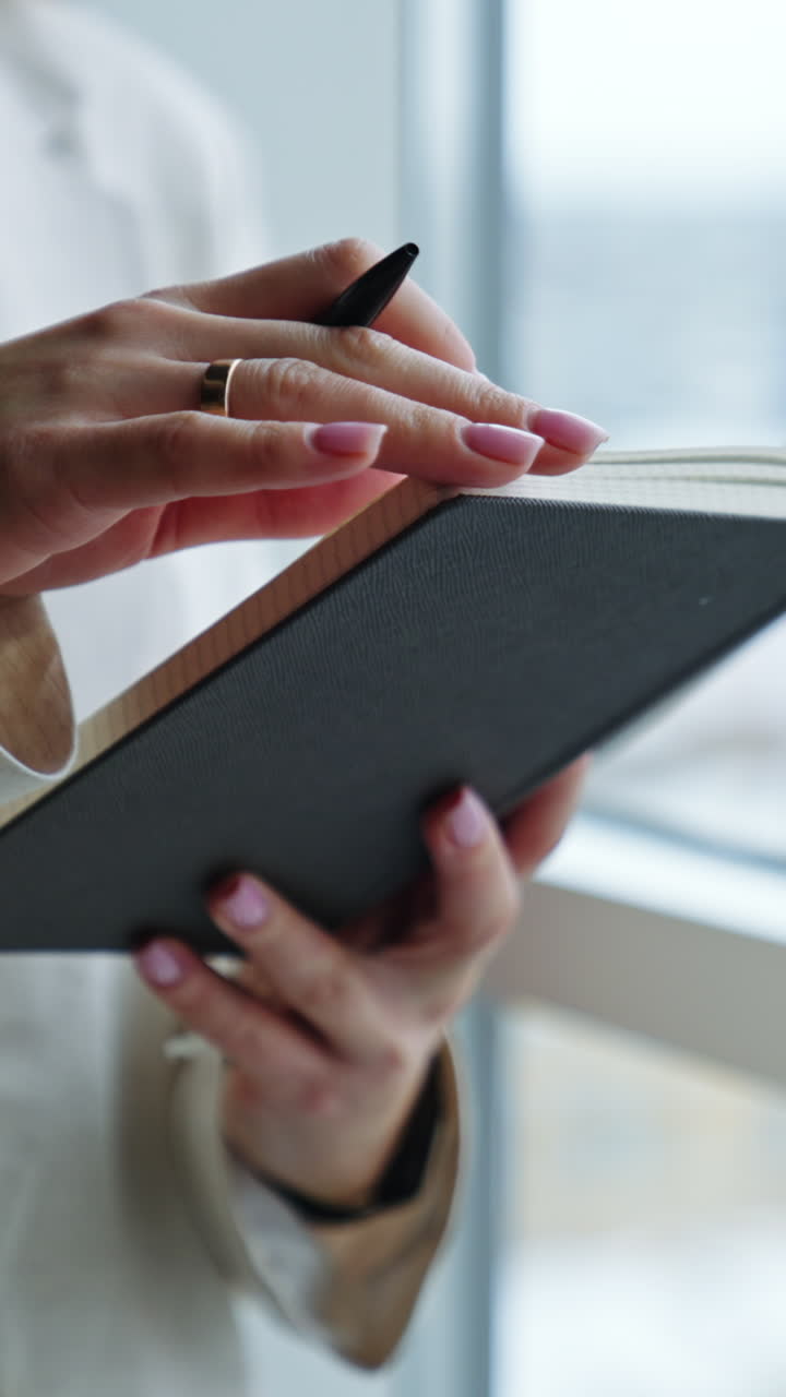 Unrecognizable woman holding a notebook in one hand and pen in another. Lady is taking notes into her book. Close up. Vertical video