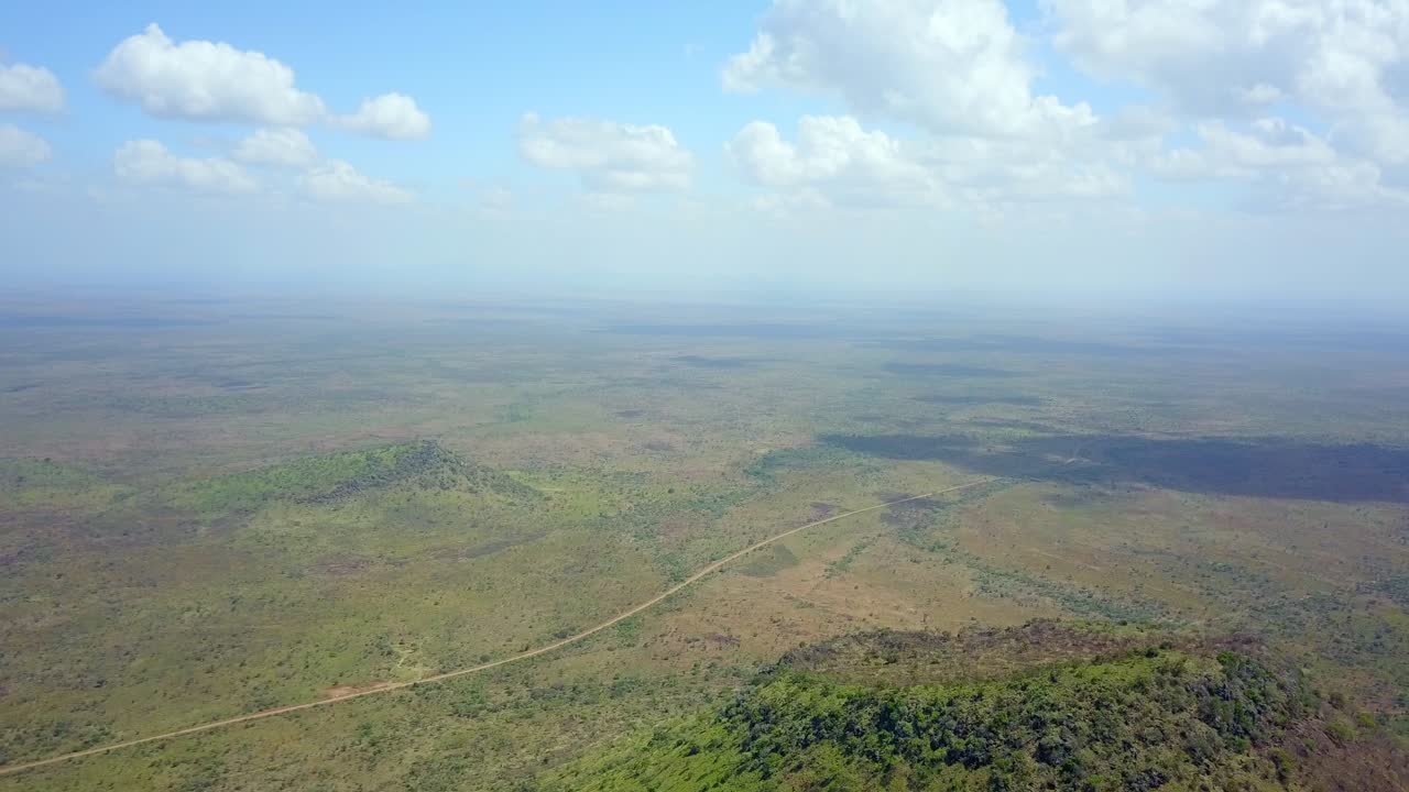 Breathtaking aerial perspective showcasing the vast, mountainous landscape of Karamoja, Uganda, featuring lush vegetation, a winding road, and a serene valley under a soft daytime sky