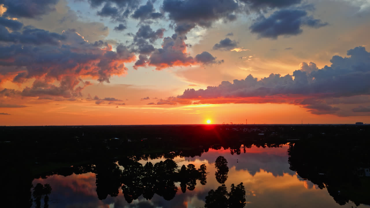 Brilliant sunset paints sky in red and orange tones over still water and forested edge, heavenly aerial backdrop background