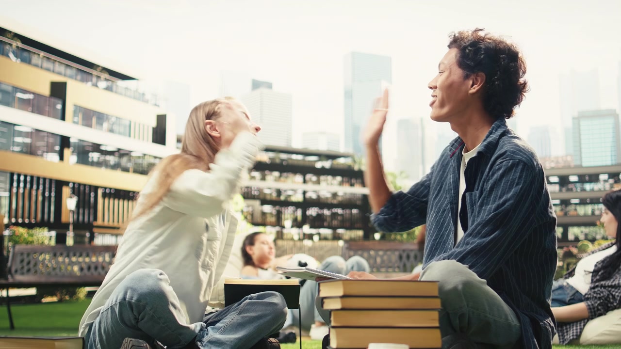 ノートパソコンと積み重ねられた本のそばで、満足げにハイタッチを交わす笑顔の学生たち