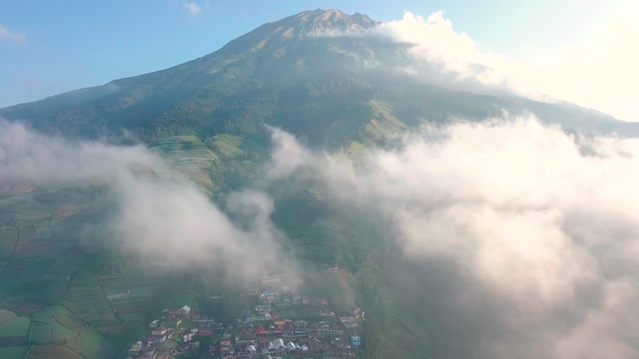 Penerbangan drone udara menembus awan menampakkan Desa Nepal Van Java dan Gunung Sumbing yang menjulang tinggi di bawah sinar matahari dan langit biru di Indonesia