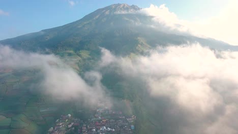 vuelo aéreo de drones a través de las nubes que revelan el pueblo de nepal van java y la montaña gigante sumergida durante la luz del sol y el cielo azul en indonesia