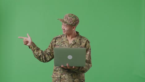 asian man soldier using a laptop and pointing to side while standing in the green screen background studio