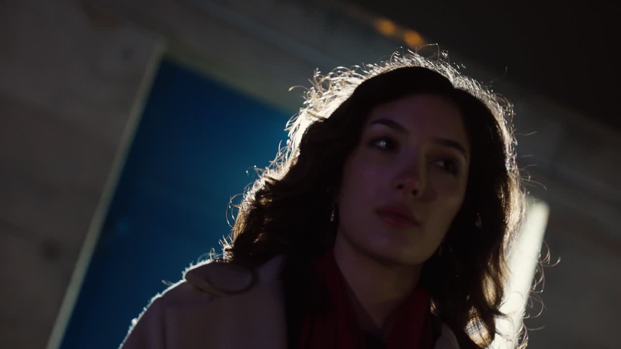 Low-angle cinematic portrait of a woman with wind moving her hair, strongly backlit to create dramatic lens flares at night. Concept for fashion film, mystery mood, and modern nightlife