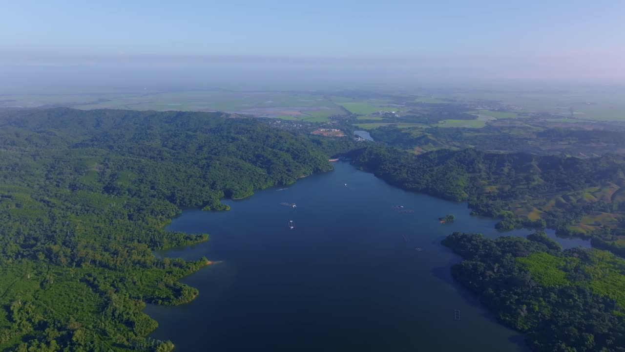 Vast Rincon dam reservoir surrounded by lush green hills and winding shorelines under clear blue sky, Dominican Republic. Sky for copy space. Aerial forward