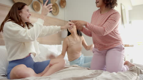 laughing and taking selfies, three diverse women friends enjoying time together on bed