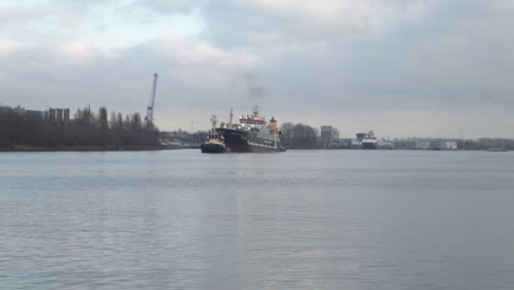 medium shot of tug boat guiding large ship over river