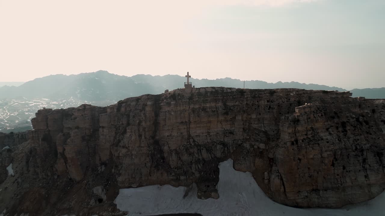 Aerial pull back drone view of cross on mountaintop to reveal Akoura church building, Lebanon