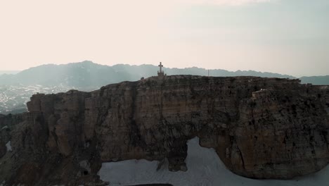 aerial pull back drone view of cross on mountaintop to reveal akoura church building, lebanon
