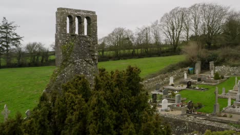 Reveal-of-old-scenic-graveyard-from-behind-tree-with-lush-green-pastures