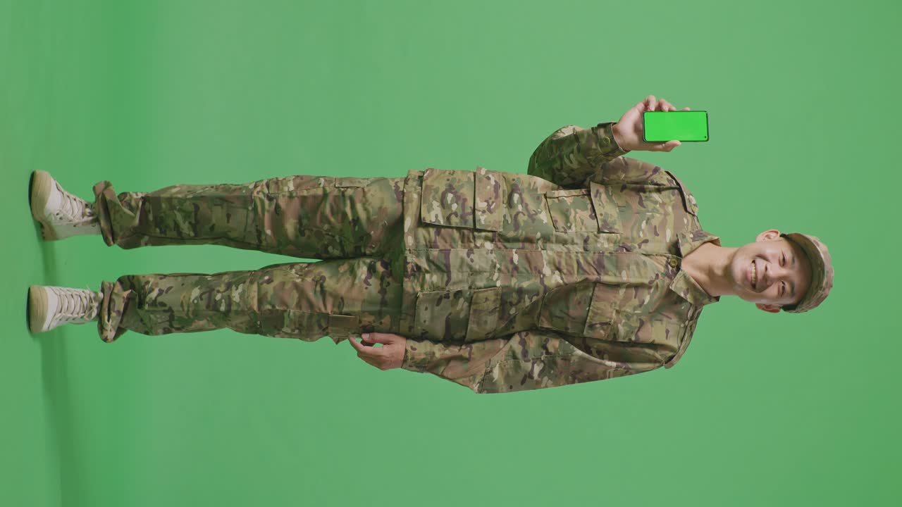 Full Body Of Asian Man Soldier Smiling And Showing Green Screen Smartphone To The Camera While Standing In The Green Screen Background Studio