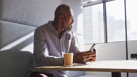 hombre de negocios afroamericano sentado en la mesa y usando el teléfono inteligente en la oficina