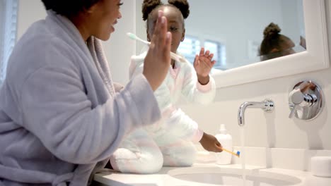 happy african american mother and daughter rinsing toothbrushes in bathroom, slow motion