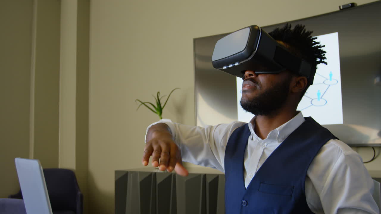 Side view of young black businessman gesturing while using virtual reality headset in office 4k