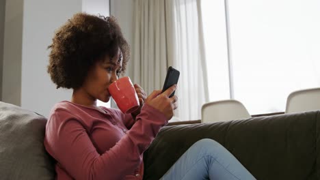 Frau-Benutzt-Smartphone-Und-Trinkt-Einen-Kaffee-Im-Wohnzimmer