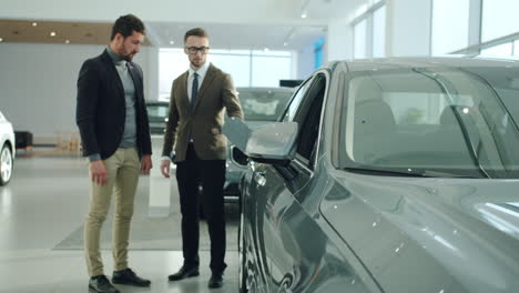 vendedor de coches mostrando el coche al cliente en la sala de exposiciones
